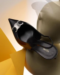 Black leather slingback pump with silver metal hardware against geometric yellow and beige abstract background.