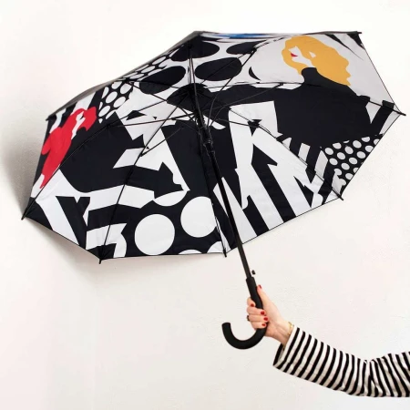 Hand holding an open umbrella featuring a black, white, and red graphic illustration against a plain white background.