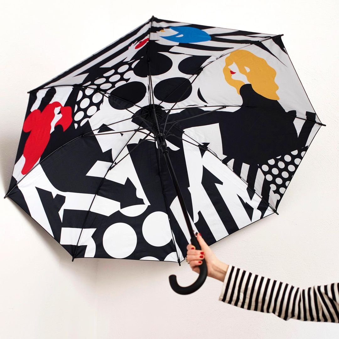 Fashionable black and white umbrella with bold pattern, featuring graphic woman and abstract shapes, held by a woman's arm in striped sleeve.