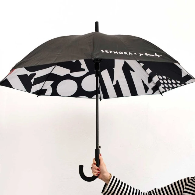 Person holding a Sephora x Joanie Charley black and white umbrella with a pattern of shapes against a white background.
