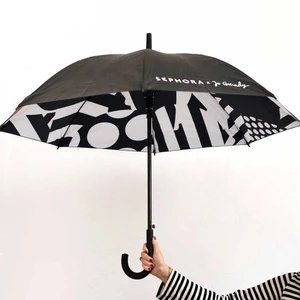 Hand holding an open black umbrella with a bold black and white patterned interior lining against a plain white wall