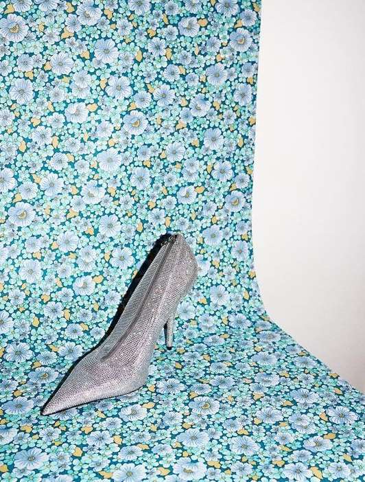 Elevated silver pointed-toe stiletto on floral backdrop. Fashionable high heel shimmers in a studio product shot.