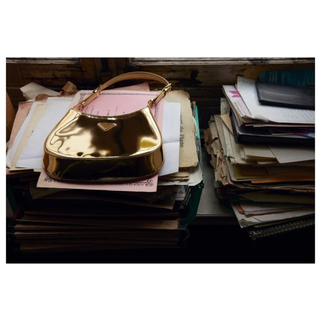 Gold Prada handbag on a stack of papers with vintage sheet music on a table, offering a glimpse into luxury fashion and historical charm.