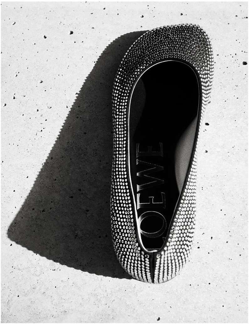 Elevated shot of a bejeweled flat shoe by Loewe set against a textured grey background with a shadow highlighting the brand's name.