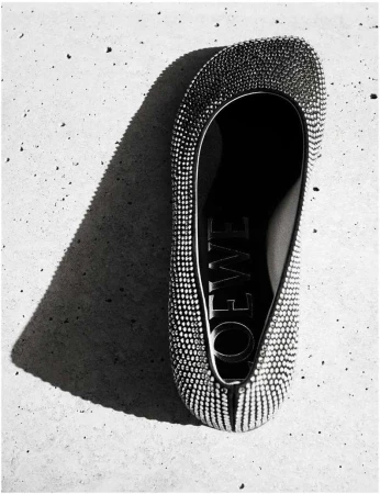 Elevated shot of a bejeweled flat shoe by Loewe set against a textured grey background with a shadow highlighting the brand's name.