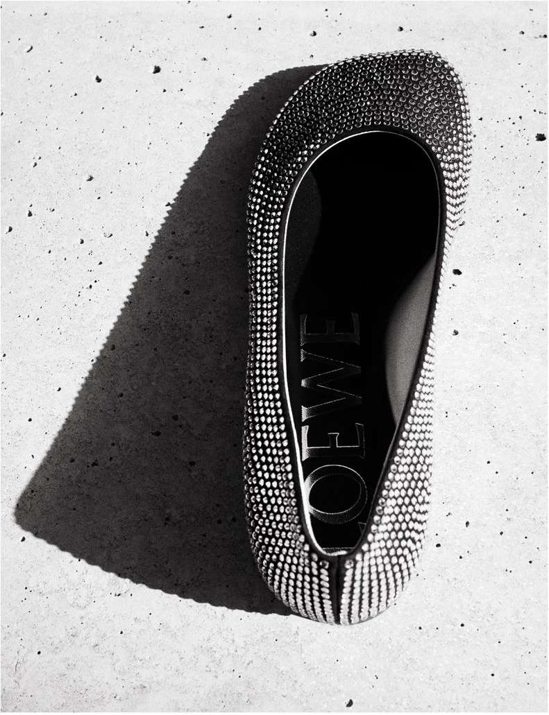 Overhead shot of a Loewe ballet flat adorned with rhinestones, casting a sharp shadow on a textured concrete surface.