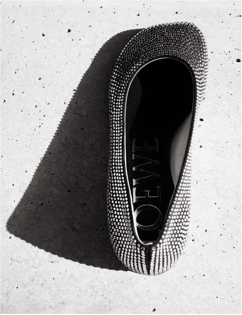 Overhead shot of a Loewe ballet flat adorned with rhinestones, casting a sharp shadow on a textured concrete surface.