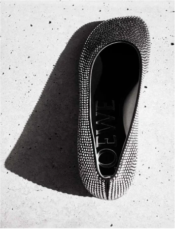 Overhead shot of a Loewe ballet flat adorned with rhinestones, casting a sharp shadow on a textured concrete surface.