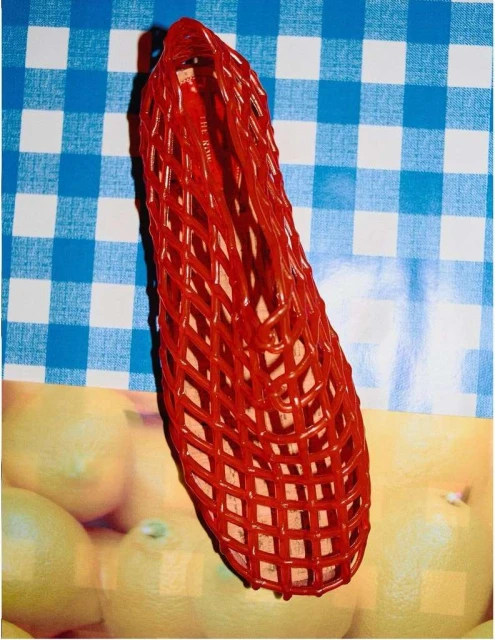 Red woven shoe on a light blue and white checked surface with lemons. The shoe has a woven design and a rounded toe.