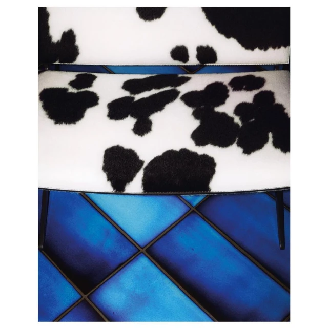 Close-up of a modern chair featuring a white cushion with a black cowhide print and a blue geometric floor pattern.
