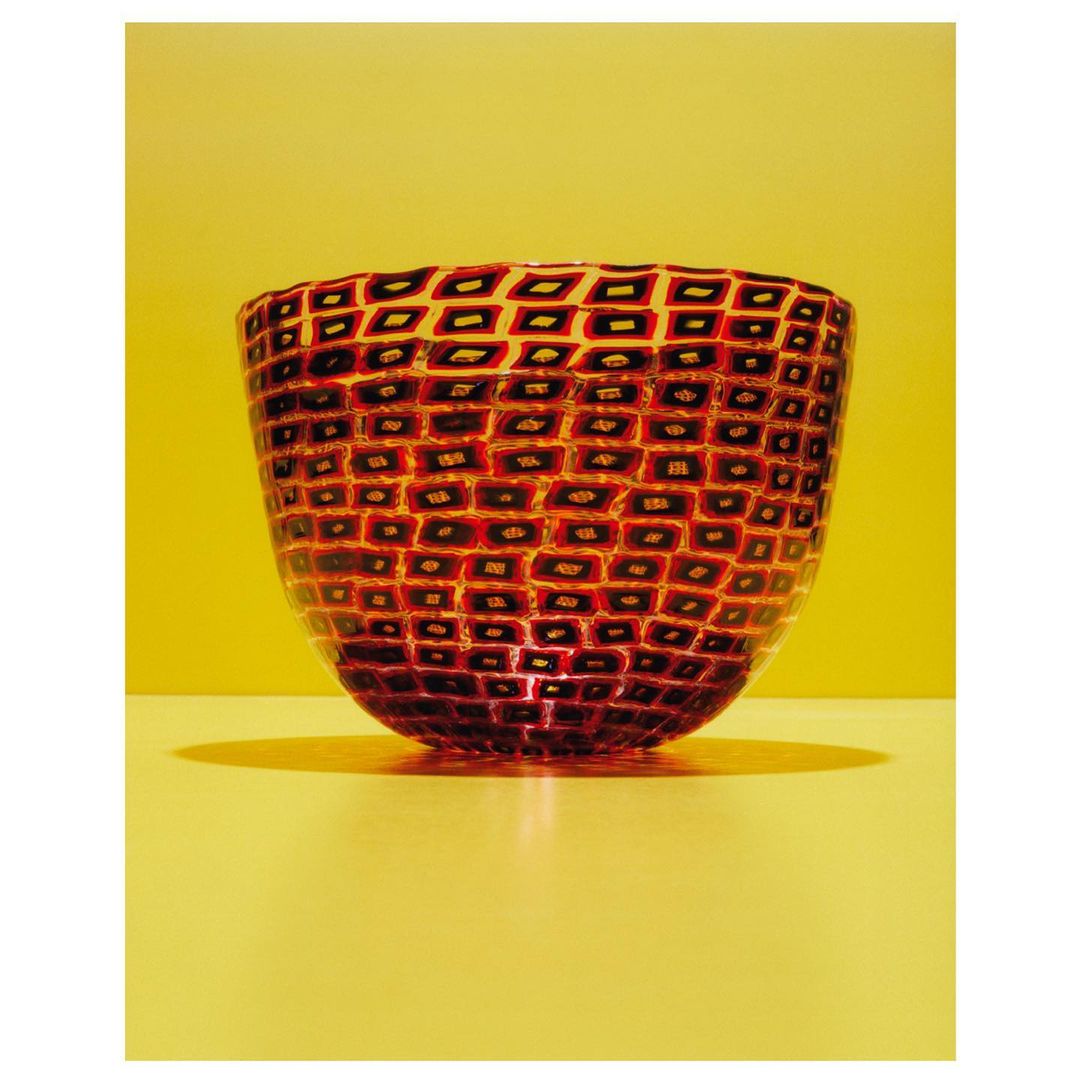 Studio shot of a red glass bowl with a geometric pattern against a yellow background, showcasing its design and craftsmanship.