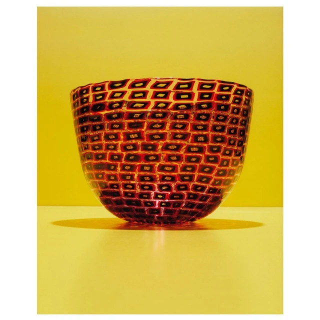 Studio shot of a red glass bowl with a geometric pattern against a yellow background, showcasing its design and craftsmanship.