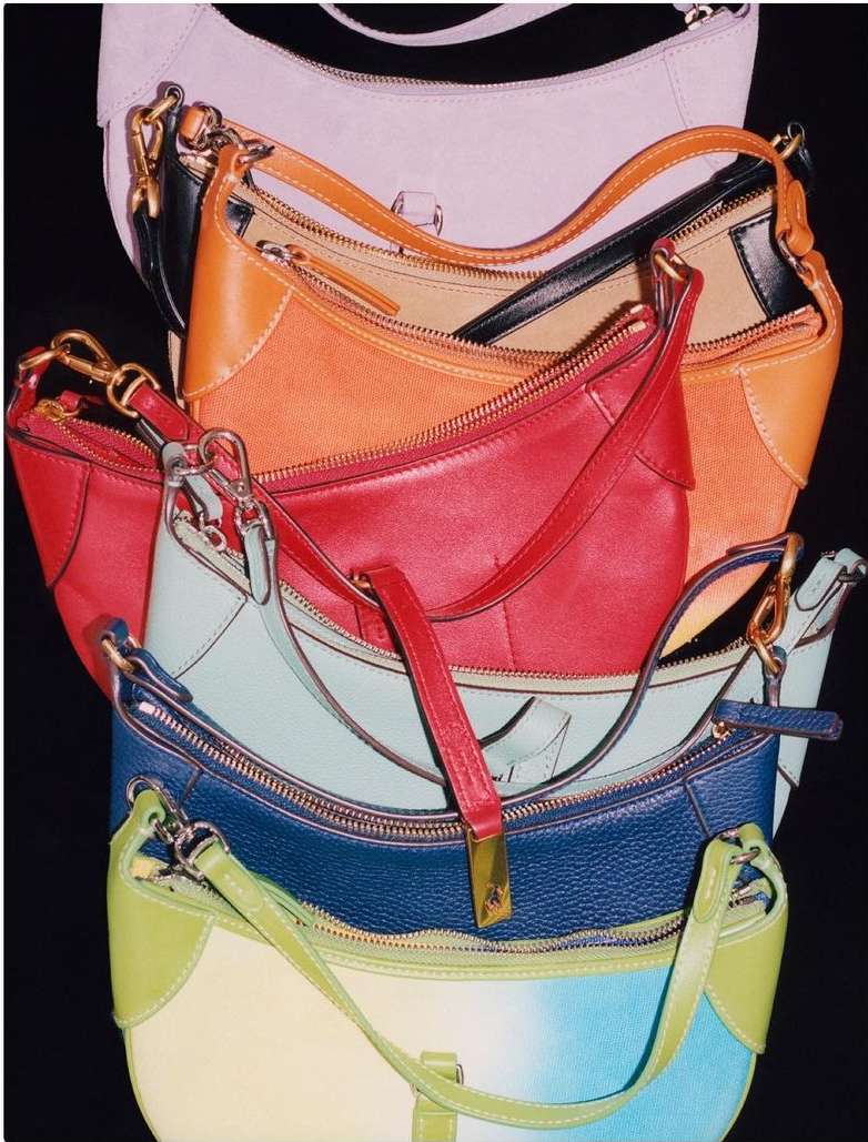 Stack of colorful baguette bags in a variety of colors including white, tan, red, teal, blue and green, against a black background.