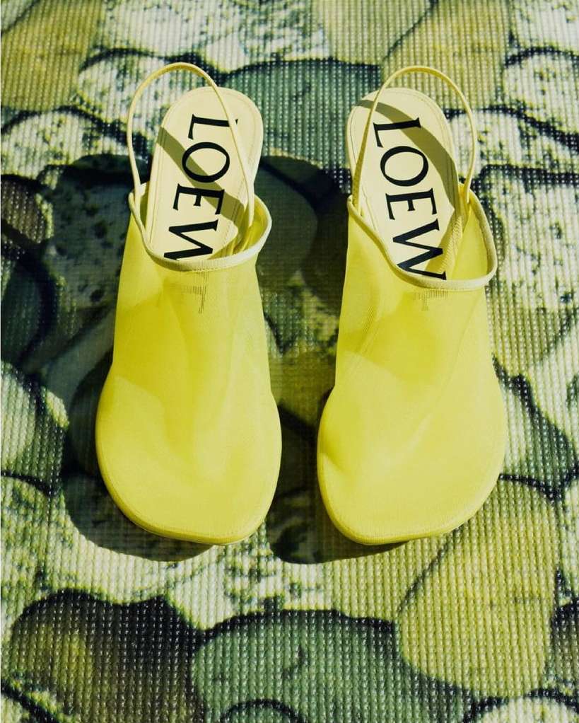 High-angle shot of a pair of yellow Loewe mule shoes with slingbacks on a patterned surface with yellow and green hues, focus on brand.