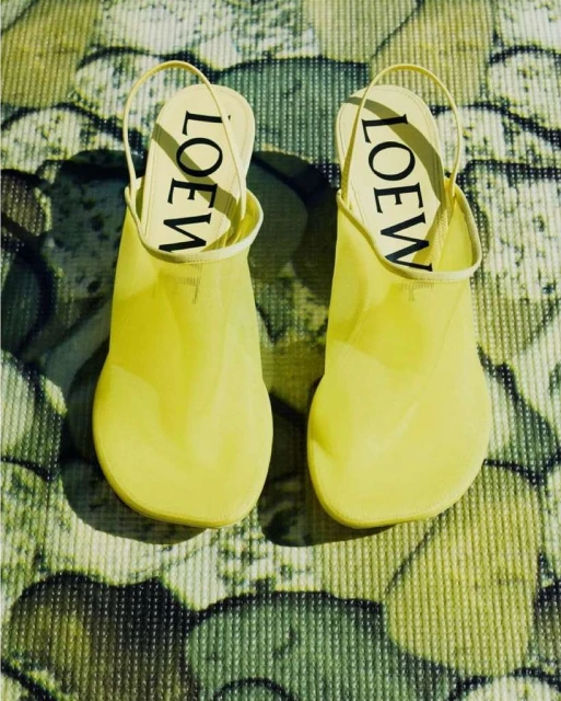 High-angle shot of a pair of yellow Loewe mule shoes with slingbacks on a patterned surface with yellow and green hues, focus on brand.