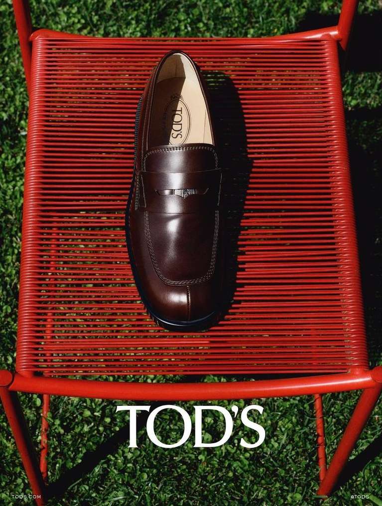 Tod's brown leather loafer on a red metal chair, set against a green grassy background, showcasing fashion and outdoor style.