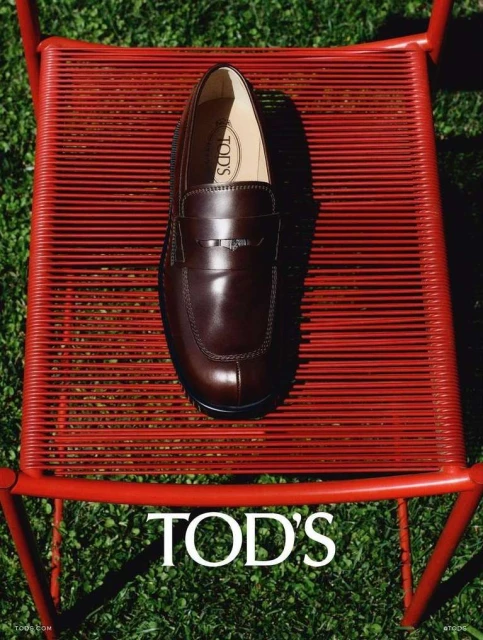 Tod's brown leather loafer on a red metal chair, set against a green grassy background, showcasing fashion and outdoor style.