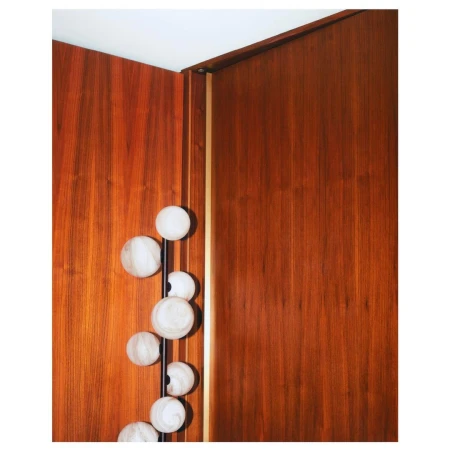 Interior architecture featuring a light fixture composed of spherical bulbs along a vertical rod against a textured wood paneled wall.