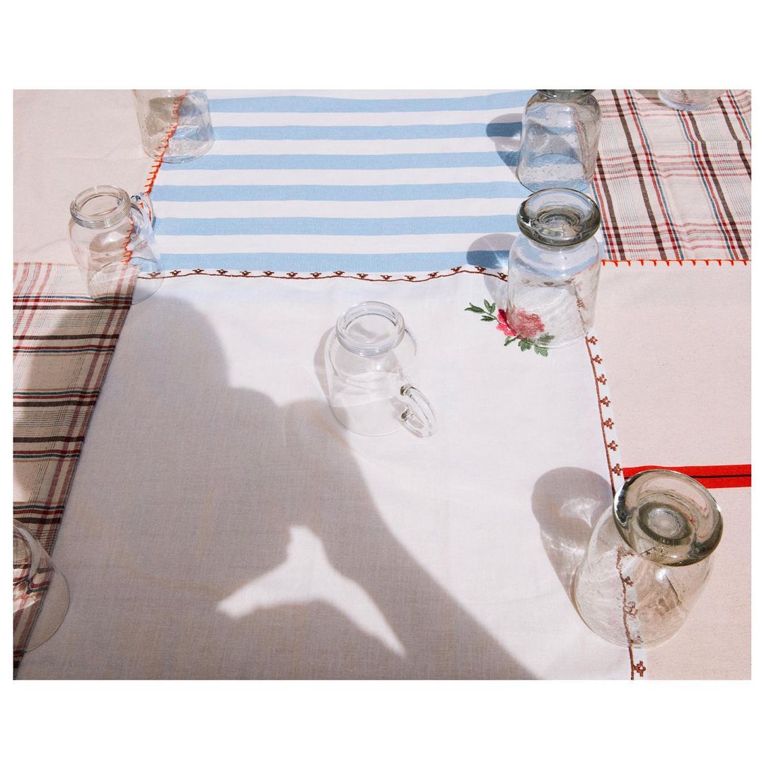 Overhead shot of clear glass jars arranged on a patterned tablecloth, with a human hand shadow reaching into the composition.