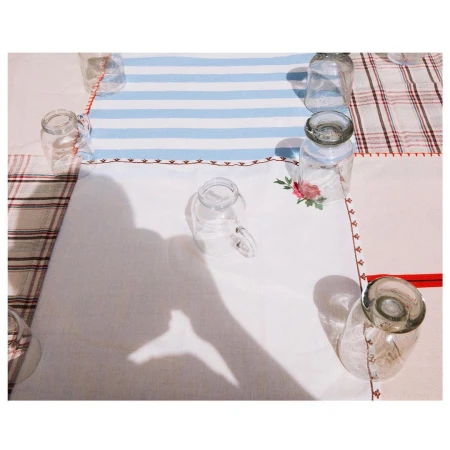 Overhead shot of clear glass jars arranged on a patterned tablecloth, with a human hand shadow reaching into the composition.