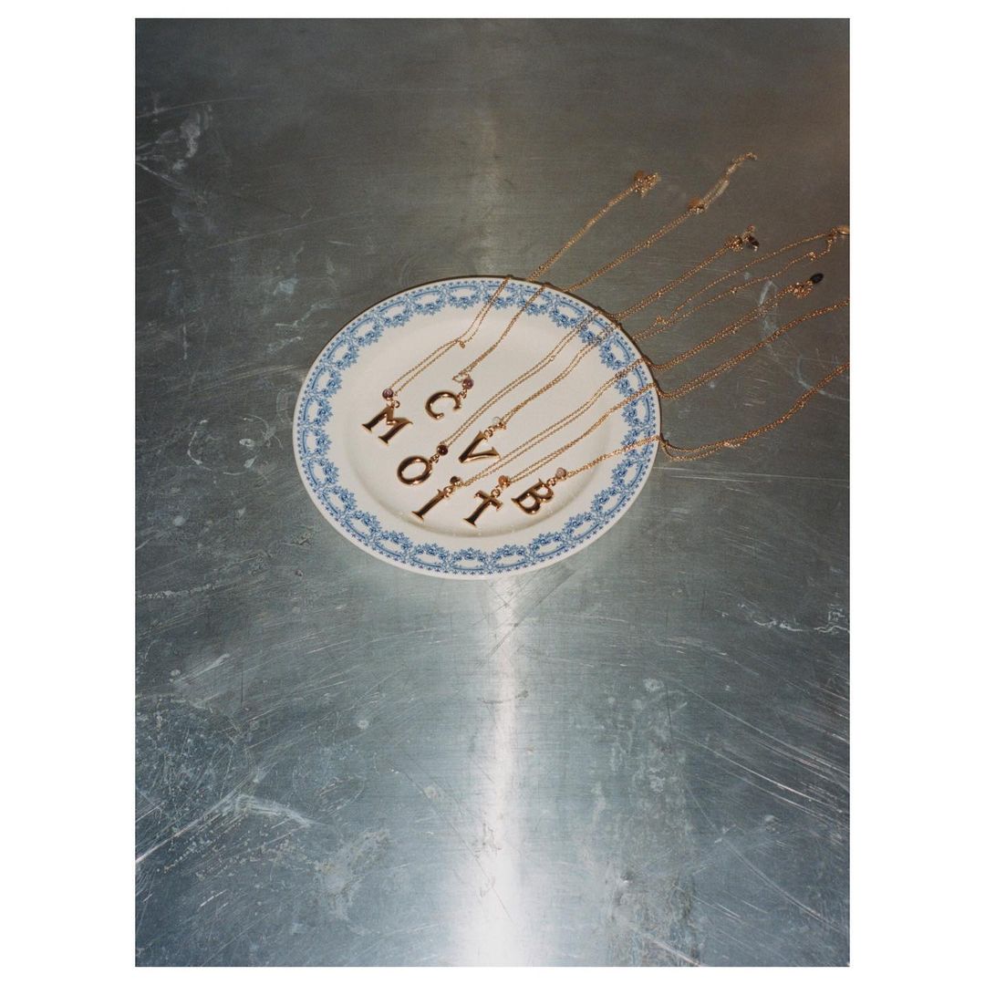 Overhead shot of letter pendant necklaces spelling out the word 'move' on a decorative blue and white plate set on a gray surface.