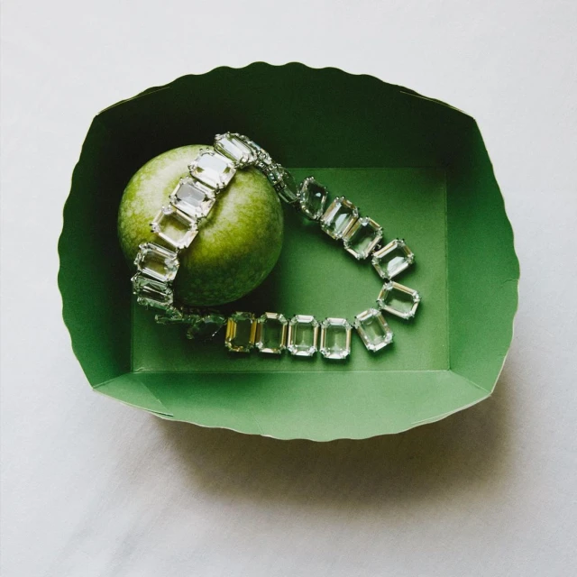 Close-up of a crystal bracelet draped on a green apple inside a green paper tray, creating a vivid colour contrast.