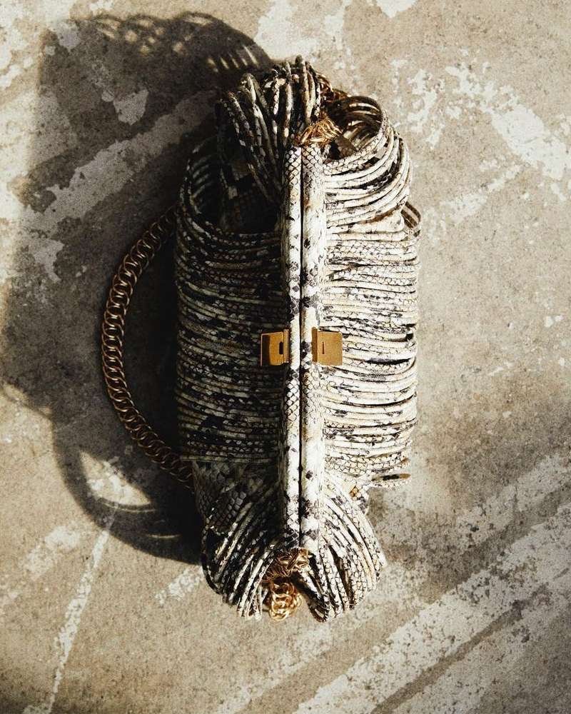 An overhead shot of a luxury snake-print purse with a gold chain handle, casting a shadow on a mottled grey surface. Fashion.