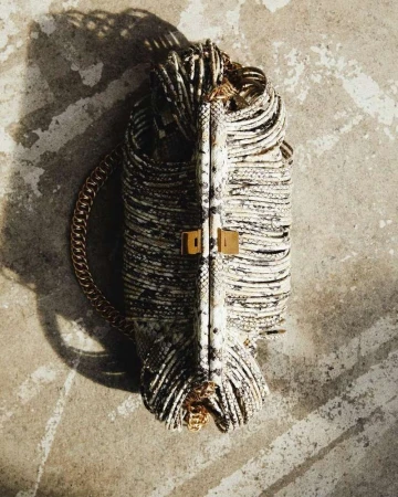 An overhead shot of a luxury snake-print purse with a gold chain handle, casting a shadow on a mottled grey surface. Fashion.
