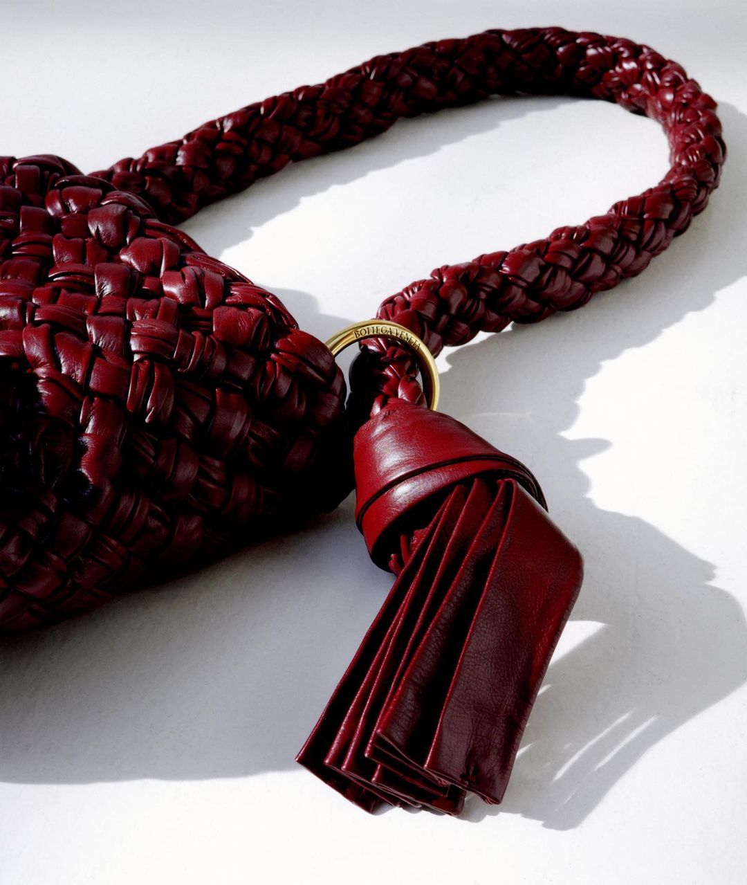 Close-up of a luxurious, woven red leather purse with a braided handle and a tassel, set against a simple, bright white backdrop.
