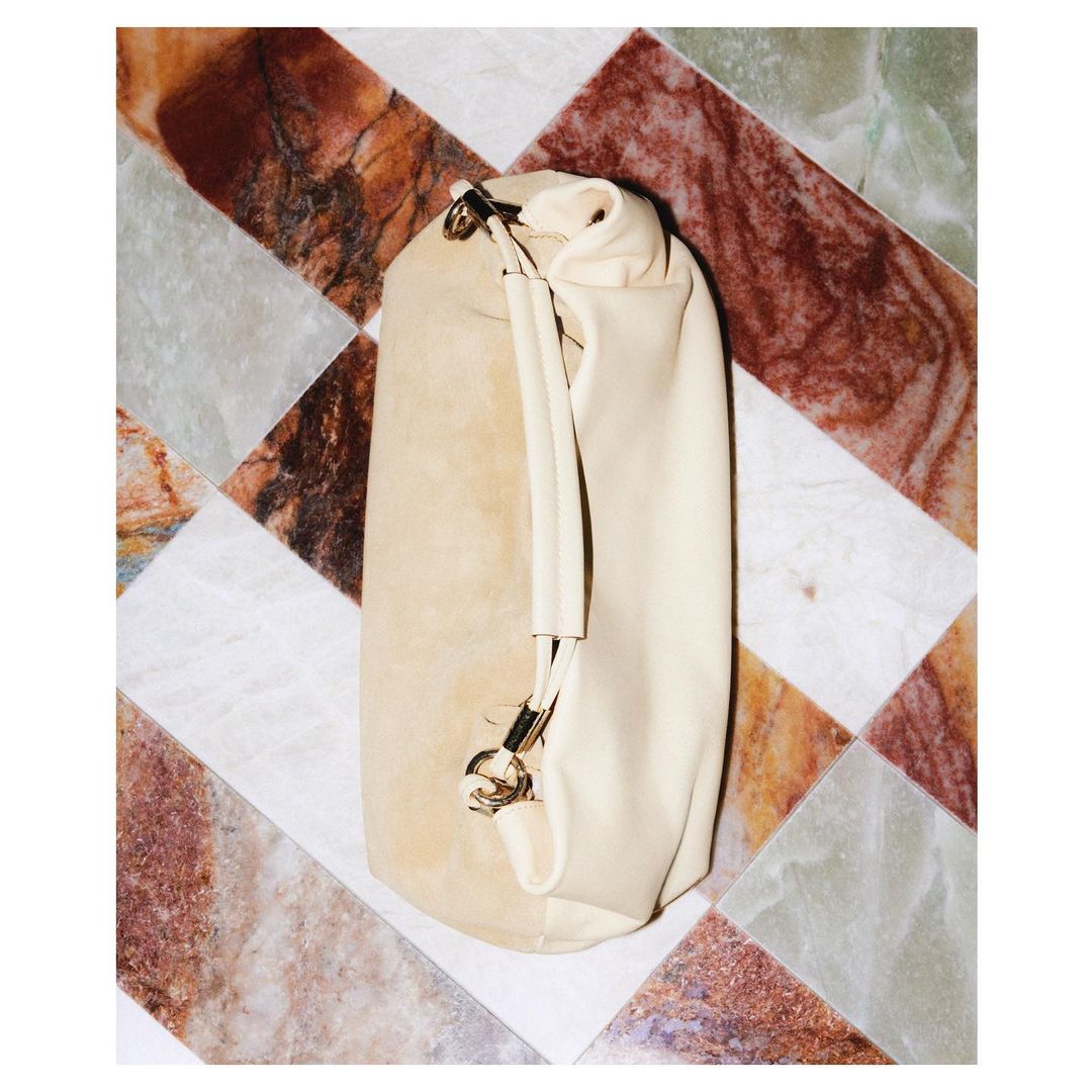 Beige leather bucket bag with a handle, displayed on a patterned marble tile surface, emphasizing luxury fashion and neutral tones.