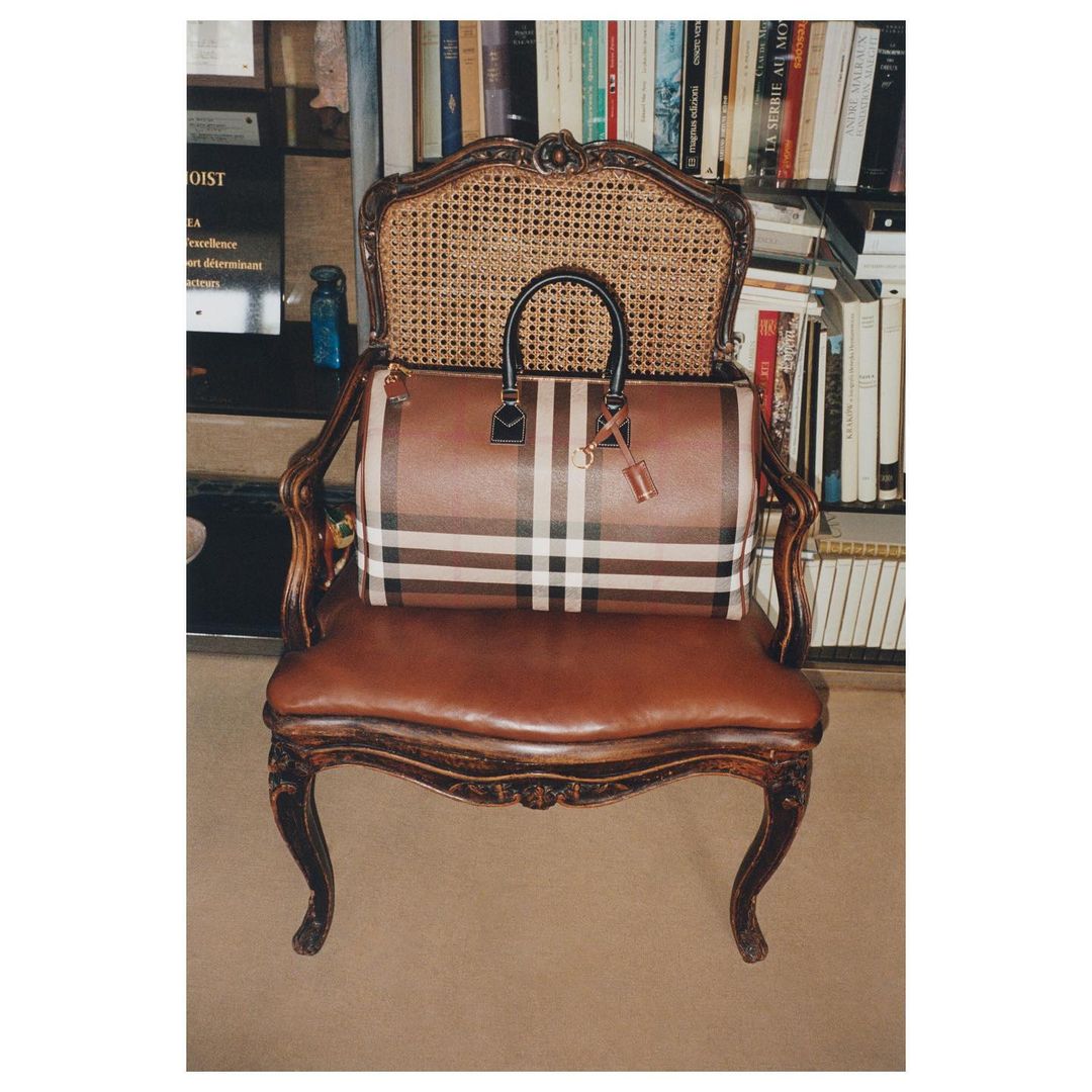 Plaid leather handbag with black handles resting on an antique wooden armchair in front of a bookshelf.