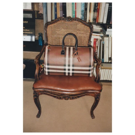 Plaid leather handbag with black handles resting on an antique wooden armchair in front of a bookshelf.