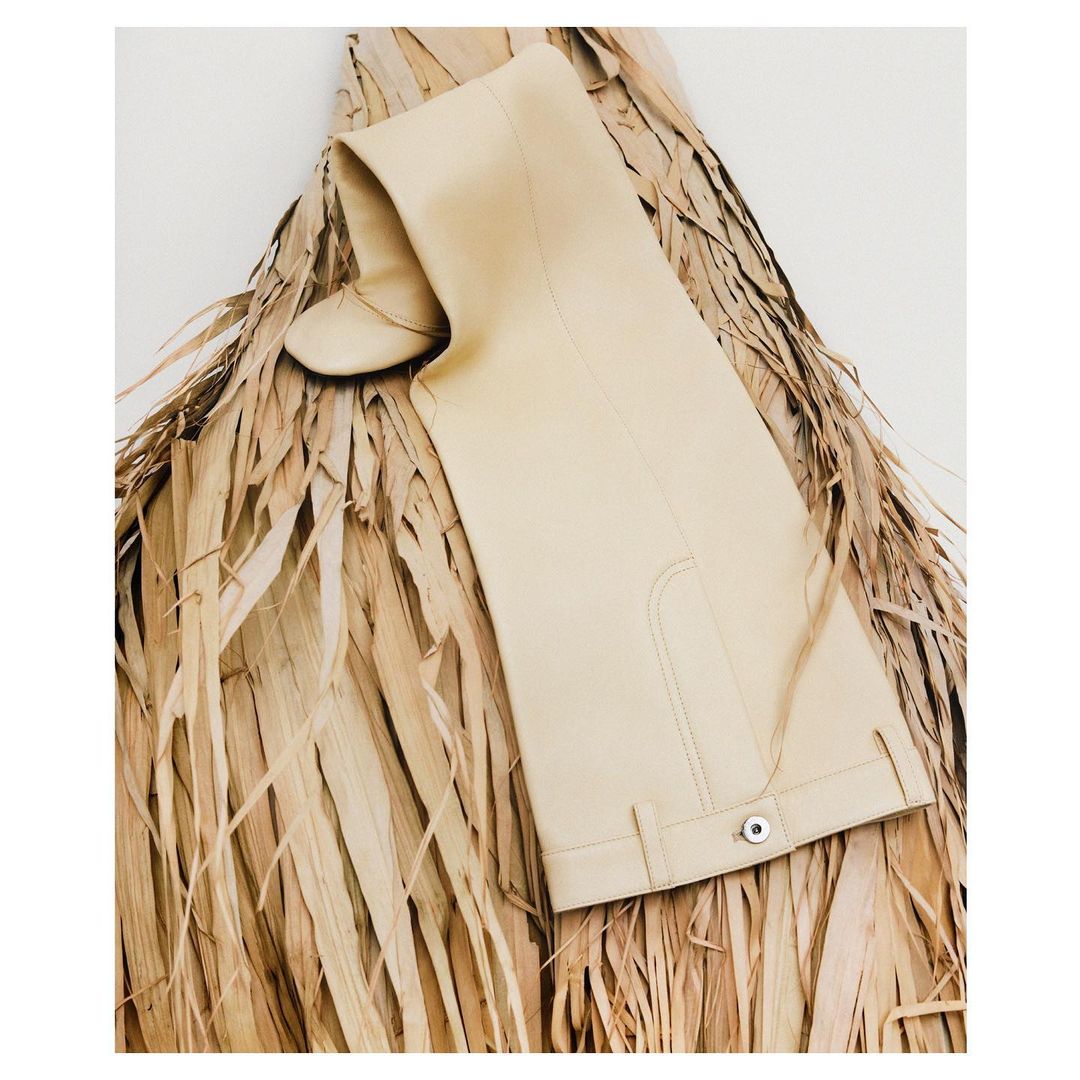 Beige over-the-knee boot on a bed of dry palm fronds against a white background, fashion editorial, studio lighting.