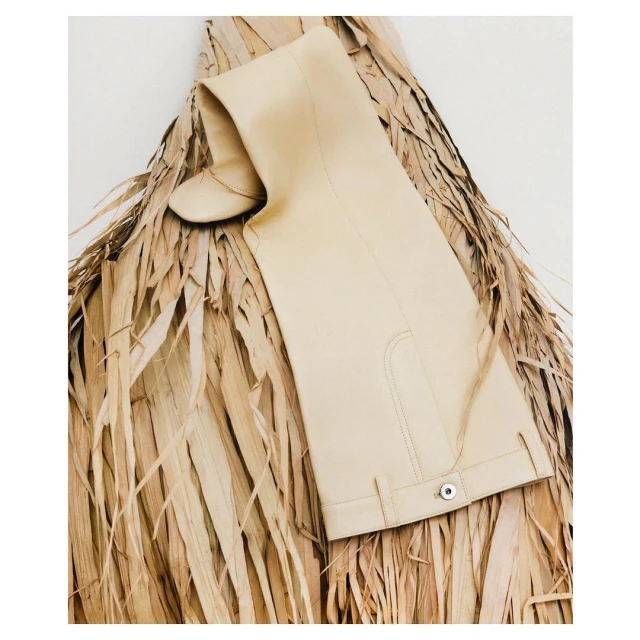 Beige over-the-knee boot on a bed of dry palm fronds against a white background, fashion editorial, studio lighting.