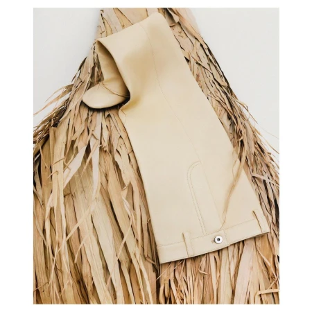 Beige over-the-knee boot on a bed of dry palm fronds against a white background, fashion editorial, studio lighting.