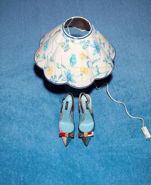 Still life shot of a floral lampshade and high heel shoes with bow on a blue carpet, product photography, home decor, fashion.