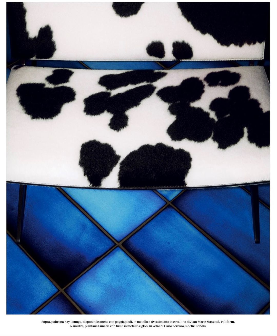 Close-up of chair with black and white cowhide pattern on seat and back, metal legs, blue quilted tile floor visible.