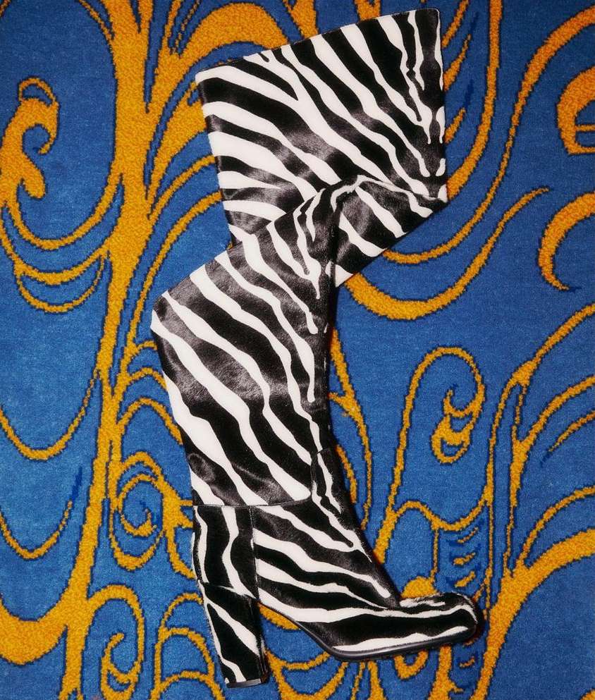 Striking zebra-striped high-heeled boot stands out on a blue and gold ornate patterned background, a fusion of fashion and art.