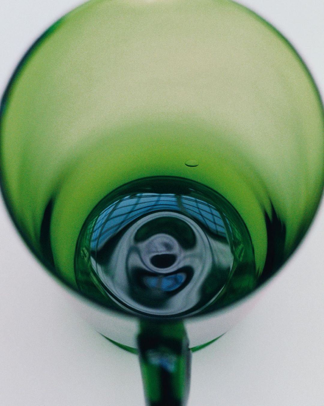 Close-up studio shot of an empty, green-tinted wine glass with a reflection in its base against a plain white background.
