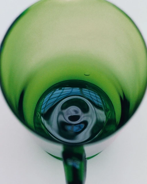 Close-up studio shot of an empty, green-tinted wine glass with a reflection in its base against a plain white background.