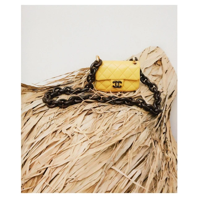 Chanel handbag in yellow quilted leather with chunky chain strap on a bed of dried palm leaves, angled close-up shot.