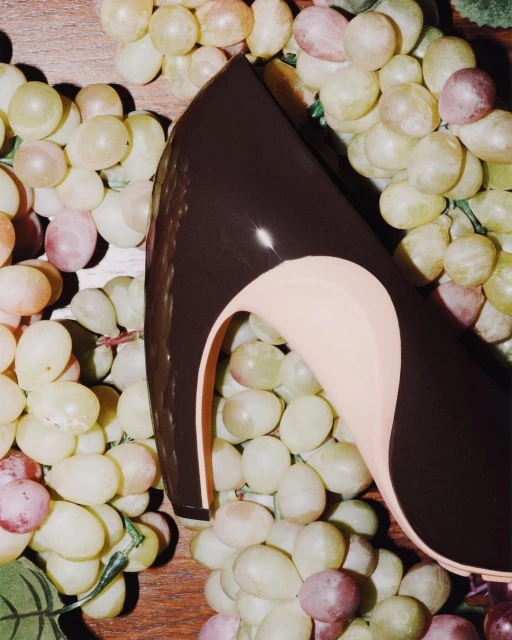 High heel shoe with brown exterior and beige interior is surrounded by clusters of green grapes, creating a fashion still life.