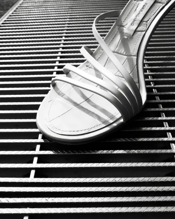Elegant white strappy sandal on a textured metal grate. High heel shoe is the central focus in this minimalist fashion shot.