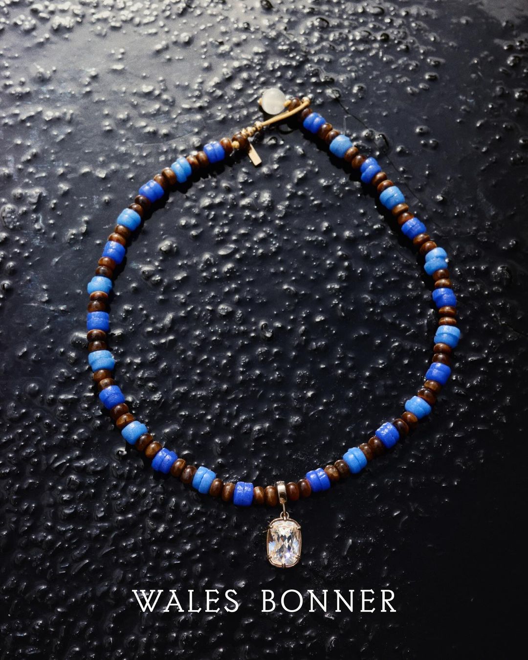 Close-up of a necklace featuring brown and blue beads and a decorative pendant, set against a dark, textured background. Fashionable jewellery.