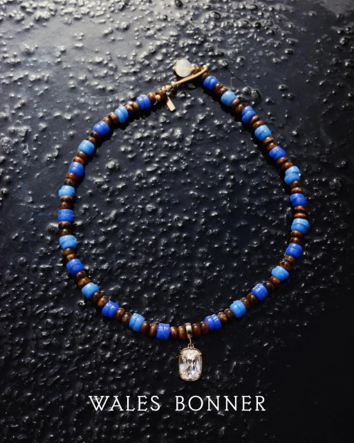 Close-up of a necklace featuring brown and blue beads and a decorative pendant, set against a dark, textured background. Fashionable jewellery.
