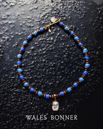 Close-up of a necklace featuring brown and blue beads and a decorative pendant, set against a dark, textured background. Fashionable jewellery.