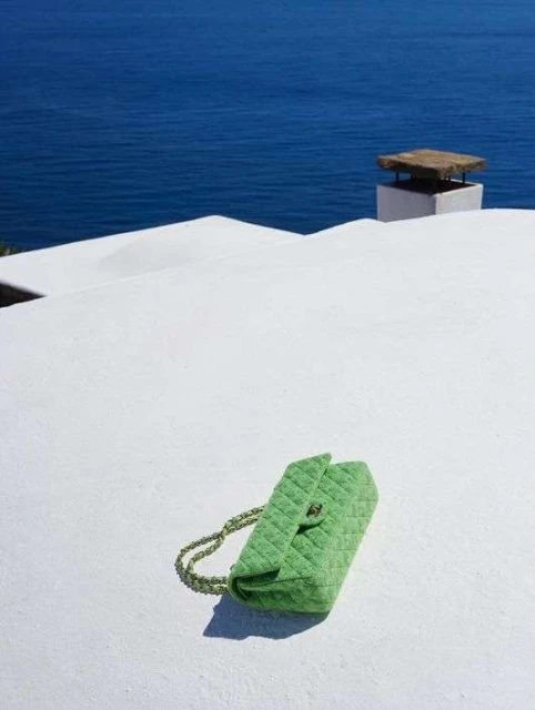 Green quilted handbag on a white surface with a blue ocean backdrop, shot on a sunny day. Perfect for fashion and travel editorials.