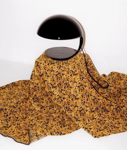 Stylish black lamp stands on a table draped with a patterned ochre and black fabric, creating a contrast against a plain white backdrop.