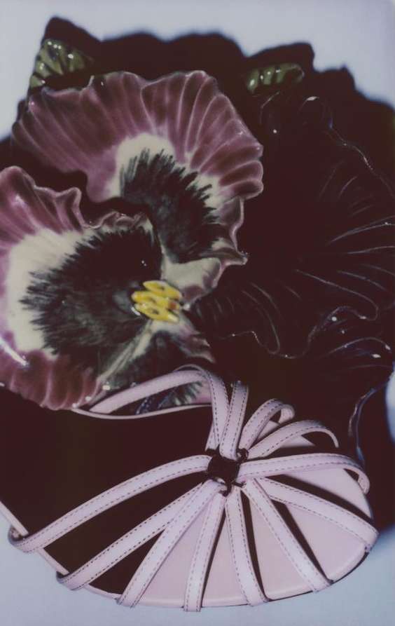Still life photograph featuring a pair of pink strappy sandals with a decorative ceramic flower, showcasing textures and colors.