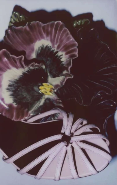 Still life photograph featuring a pair of pink strappy sandals with a decorative ceramic flower, showcasing textures and colors.